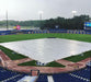 Baseball field with a tarp over it, surrounded by stadium seating and advertisements.